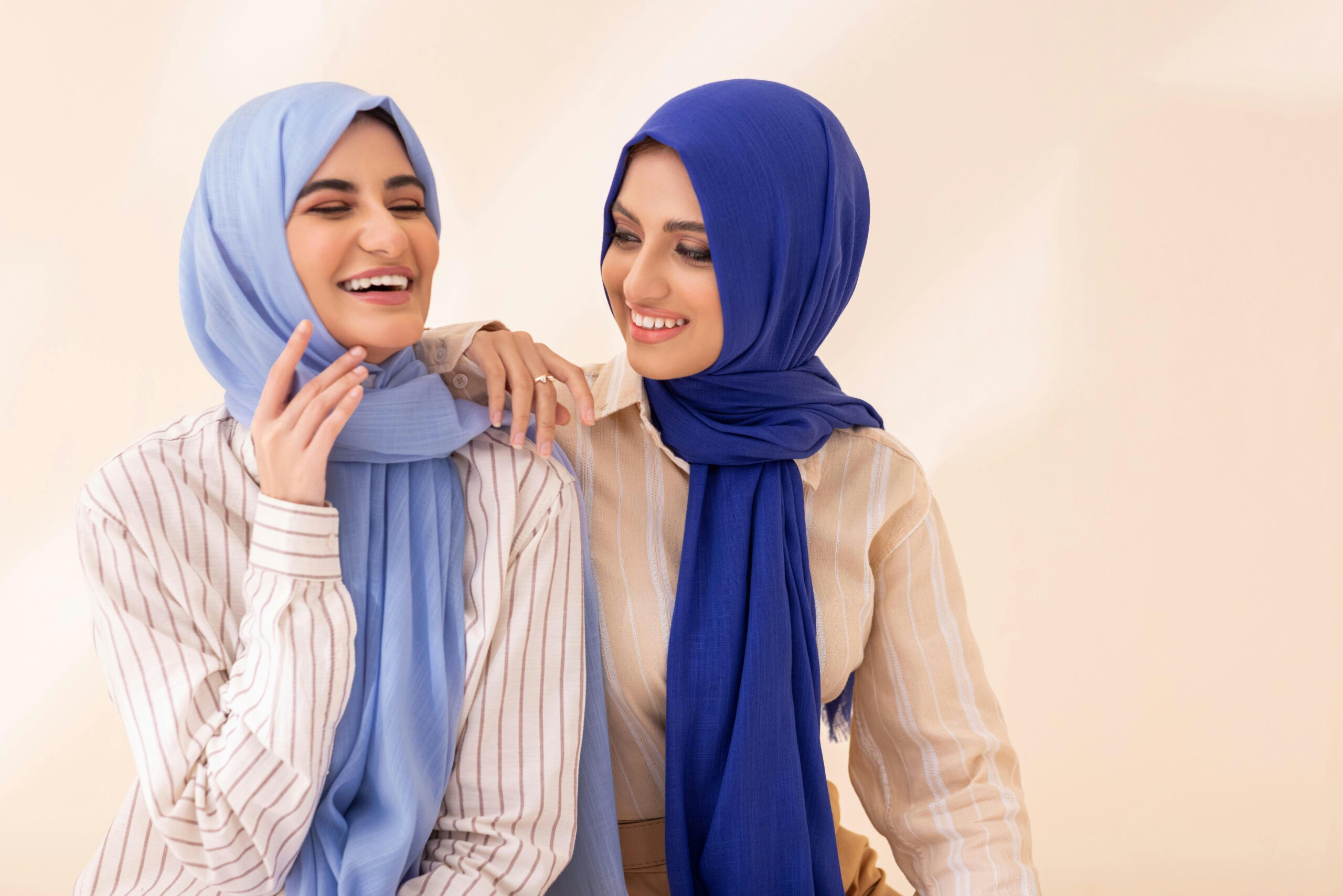 Cheerful women in blue hijabs enjoying a light moment indoors.