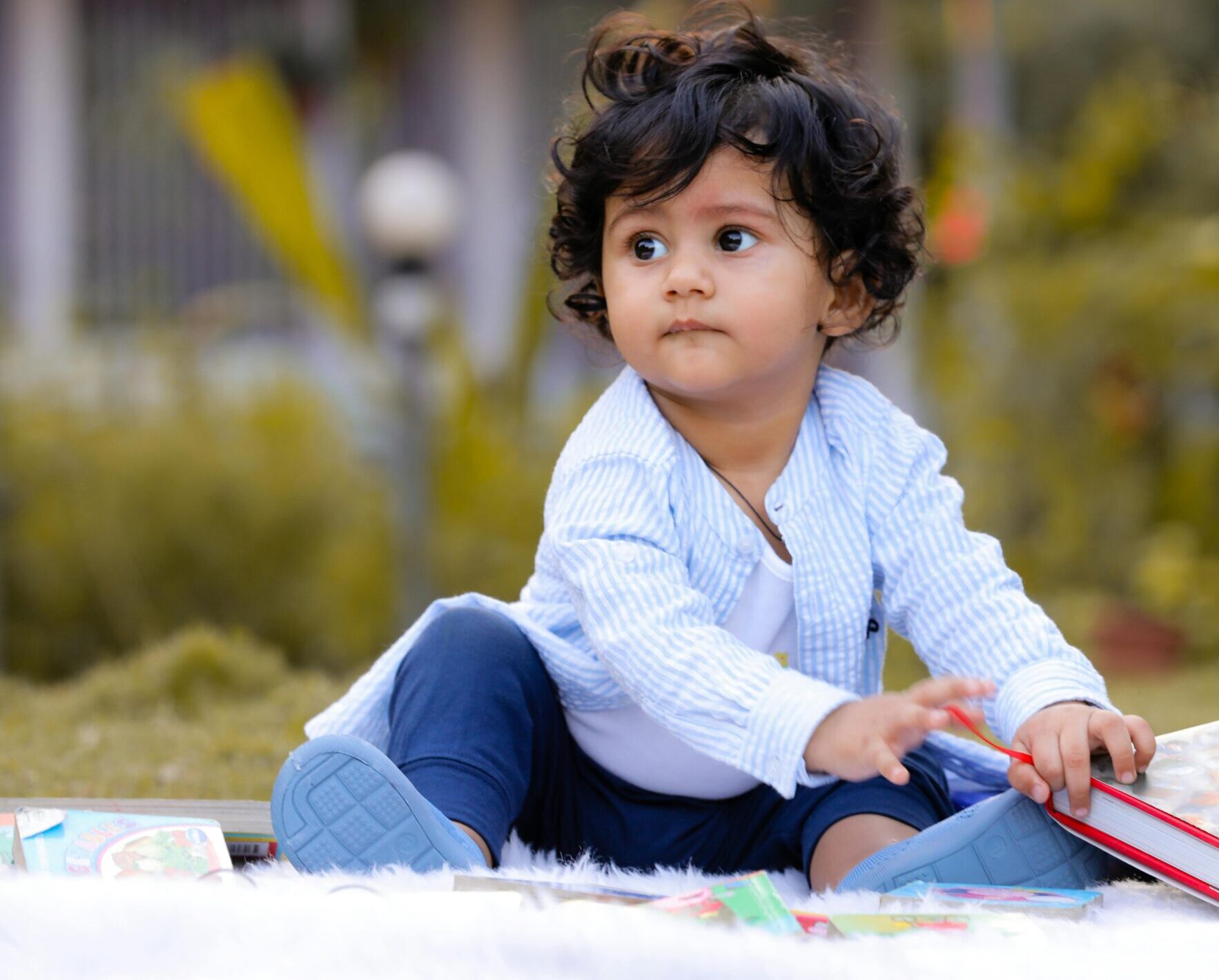 Adorable toddler sitting outdoors in Bhavnagar, India, enjoying a picture book on a sunny day.