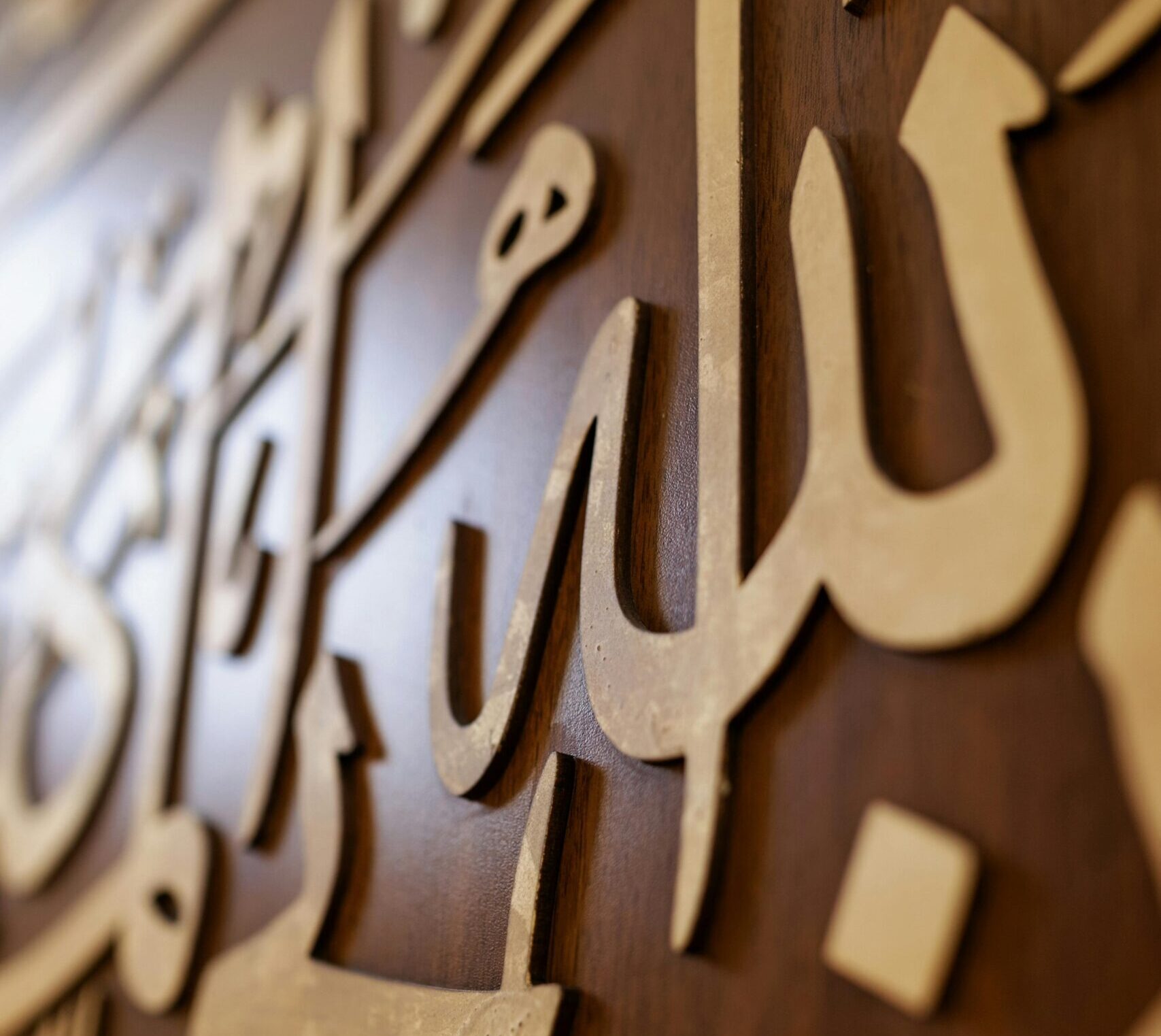 Close-up of ornate Arabic calligraphy on a wooden wall, highlighting Islamic artistry.