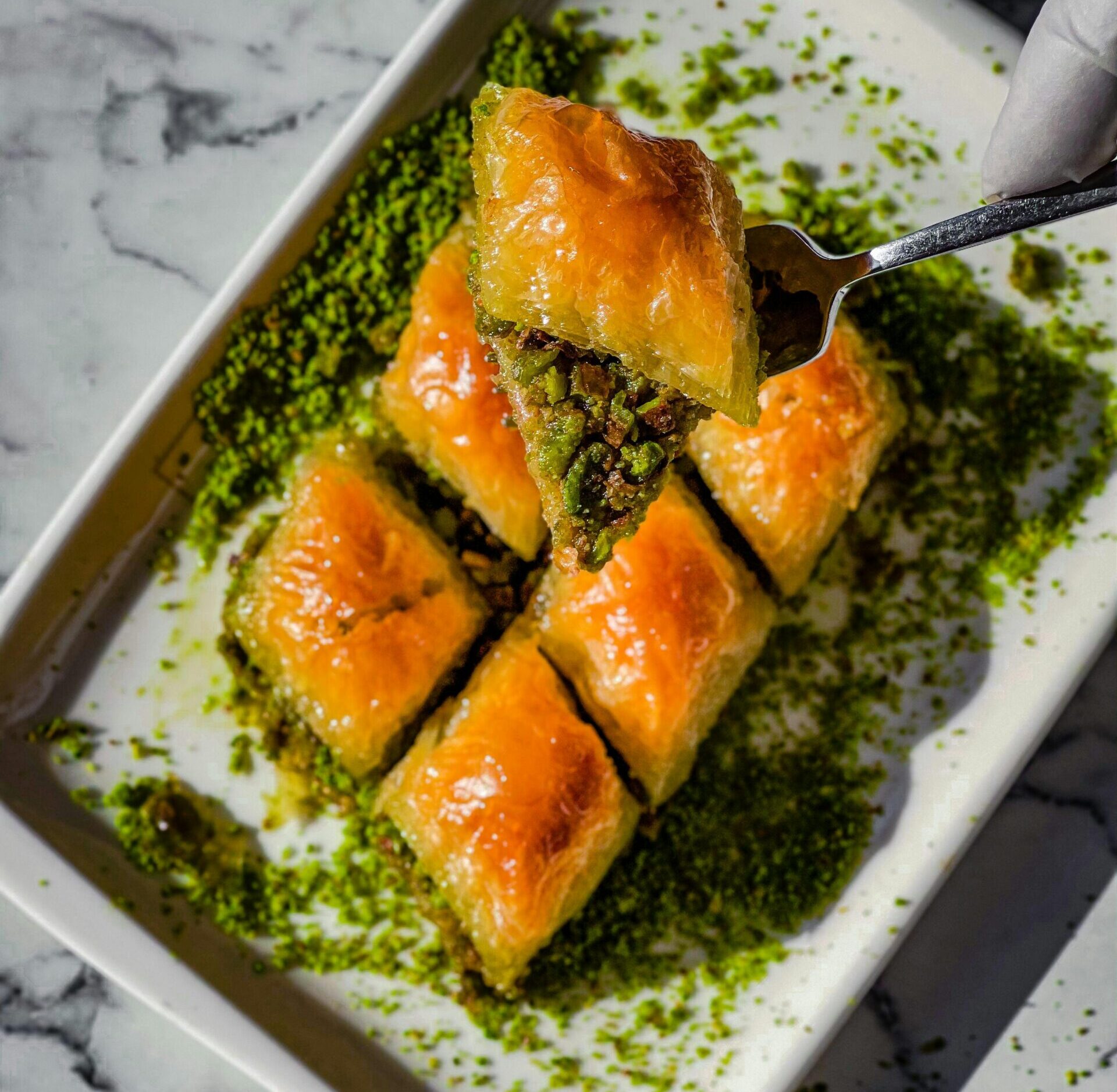 Close-up of golden baklava slices with pistachio on a marble background, presented on a white plate.